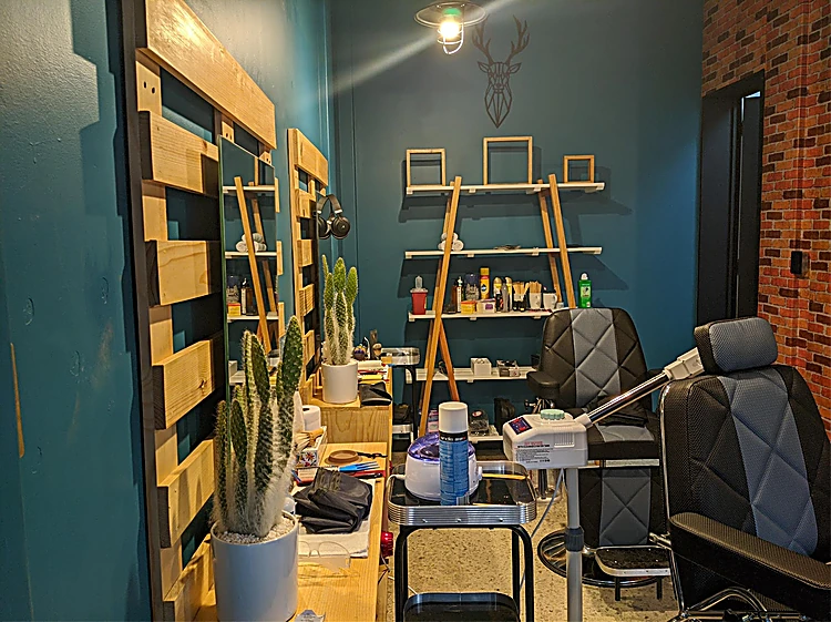 Interior de la barbería: muro azul petróleo, repisas de tarima con productos, cabeza de venado de adorno, sillones negros y muro de ladrillo