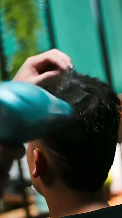 Barbero peinando y secando el cabello de un cliente, visto de espaldas